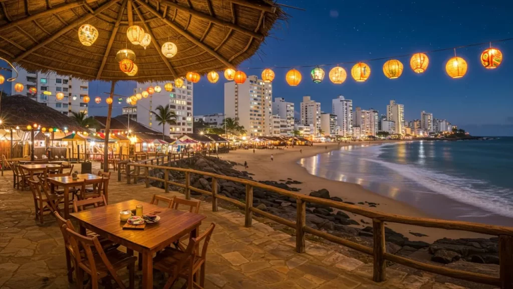 Descubra o Charme do Turismo de Inverno em Guarapari: Além do Sol e Praia 2 Turismo de Inverno em Guarapari: Ambiente noturno acolhedor de um restaurante à beira da Praia do Morro em Guarapari, com mesas e cadeiras de madeira sob um toldo de palha, decorado com lanternas coloridas iluminadas, a praia com poucas pessoas e os prédios da orla ao fundo sob um céu estrelado.