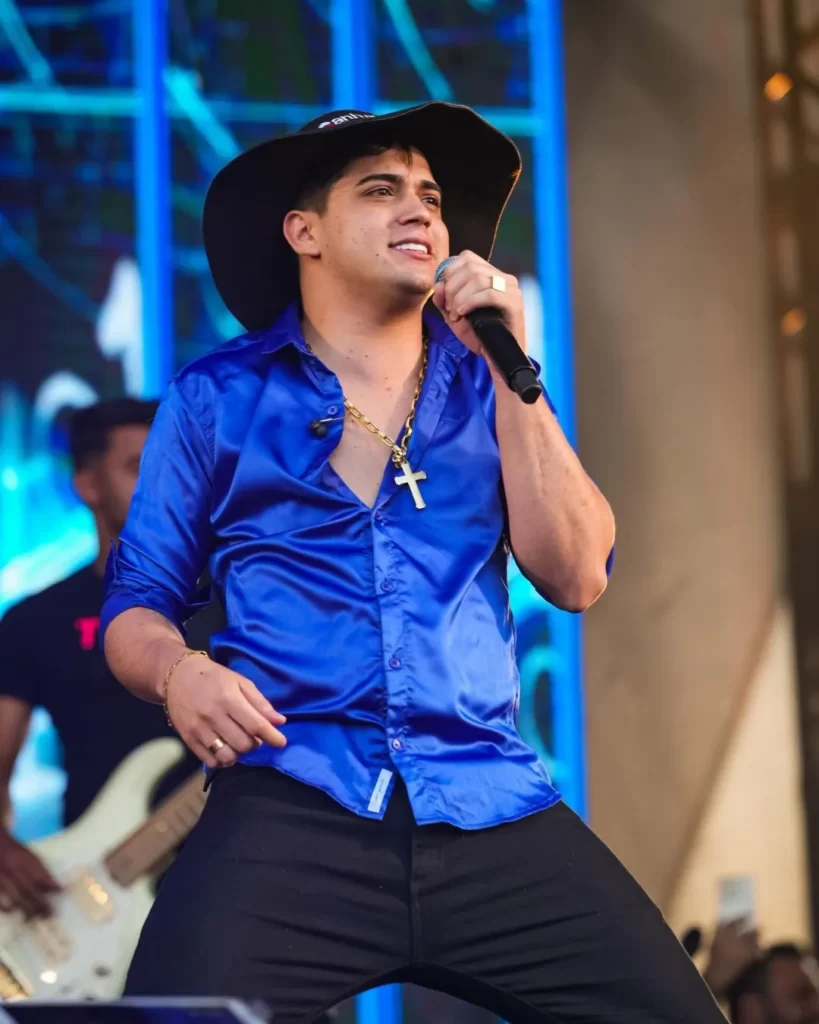 Show de Natanzinho Lima na Expo Aracruz 2025:  Natanzinho Lima performando com energia no palco, segurando o microfone e interagindo com a plateia, iluminado por luzes de show durante o evento em Aracruz.