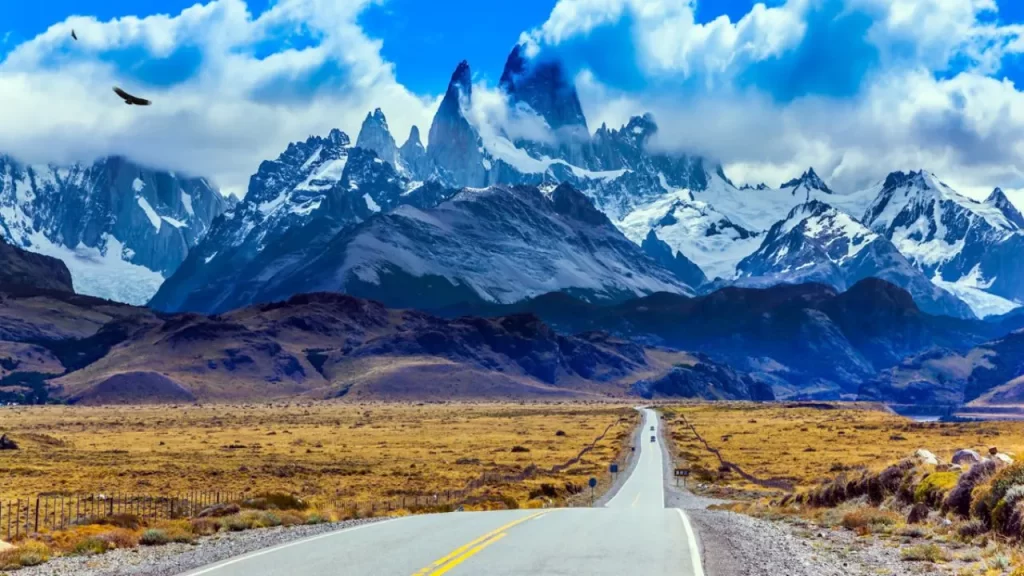 Destinos de Viagens Top: Um Guia Completo para Planejar Sua Próxima Aventura Inesquecível 3 Destinos de Viagens Top pelo Mundo: Longa estrada reta cortando paisagem árida em direção a montanhas altas e nevadas sob céu com nuvens dramáticas.