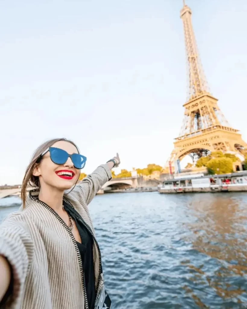 Como funciona o RCI viagens? Guia completo para transformar sua propriedade de férias em experiências incríveis 1 Uma mulher de óculos de sol, sorrindo e apontando para a Torre Eiffel, em uma selfie. Saiba como funciona o RCI viagens para visitar os destinos mais famosos do mundo.