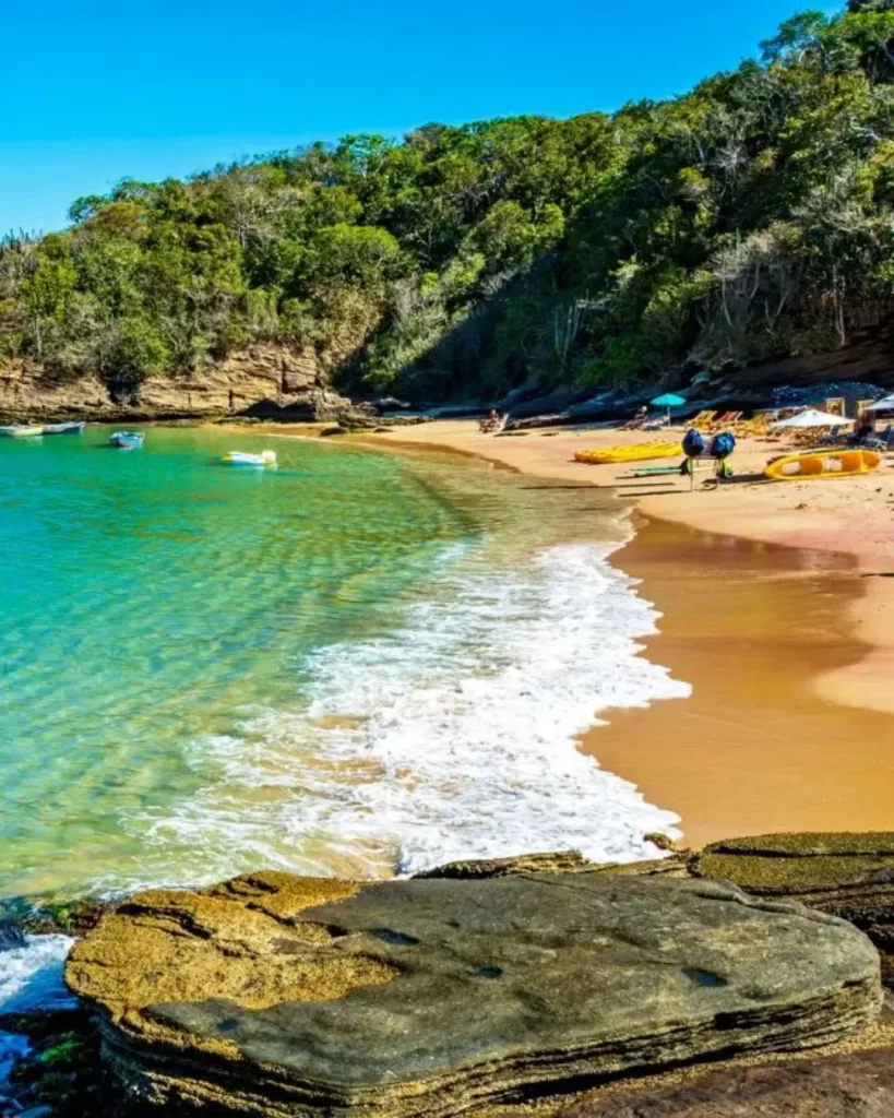 Búzios, RJ: o guia completo para encontrar o refúgio ideal com vista para o mar 4 Uma vista da praia de Búzios, RJ, com água azul-turquesa, algumas embarcações flutuando e uma costa rochosa.