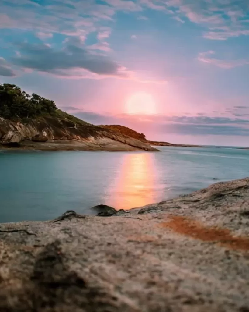 Guarapari em 3 Dias: Uma vista espetacular do pôr do sol na Praia do Ermitão em Guarapari, com o sol se refletindo nas águas calmas. Perfeito para o roteiro de 3 dias.