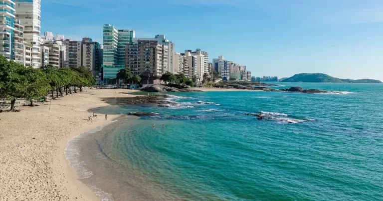 Vista panorâmica da Praia das Castanheiras em Guarapari, com suas piscinas naturais, coqueiros e prédios ao fundo. Um destaque no roteiro de 3 dias pela cidade.