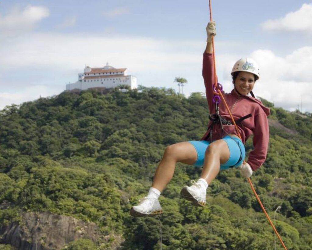 Morro do Moreno: Um guia completo para trilhas, atividades e o nascer do sol 3 Uma foto de uma das atividades mais populares, como um parapente ou asa-delta no ar, com a vista da cidade ao fundo. Isso ilustra a parte de aventura do seu guia.